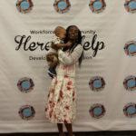 Annual Tea Party 2017 — woman holding baby at Here's Help backdrop