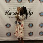Annual Tea Party 2017 — woman holding baby at Here's Help backdrop